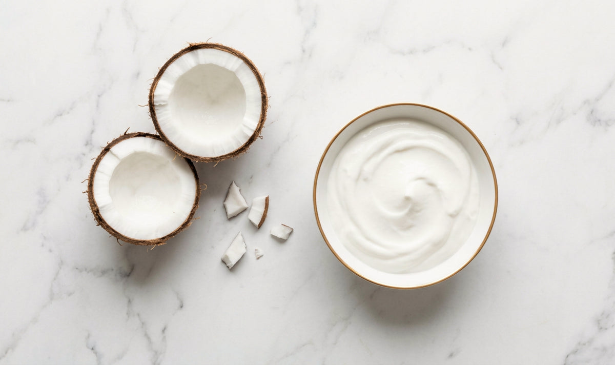A bowl of coconut-based cultured food beside a split coconut on marble